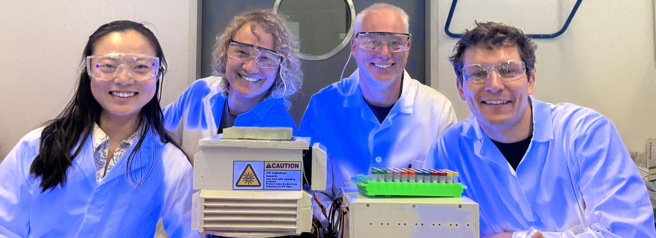 4 researchers in lab coats standing around lab equipment